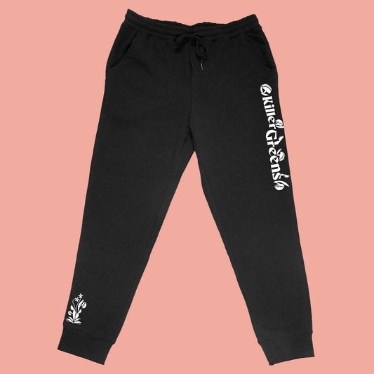 Killer Greens sweatpants. White long logo down left upper leg, small plant element above right leg cuff. Black unisex, ethically-made mid-weight fleece pants. Front view. by BBJ / Glitter Garage