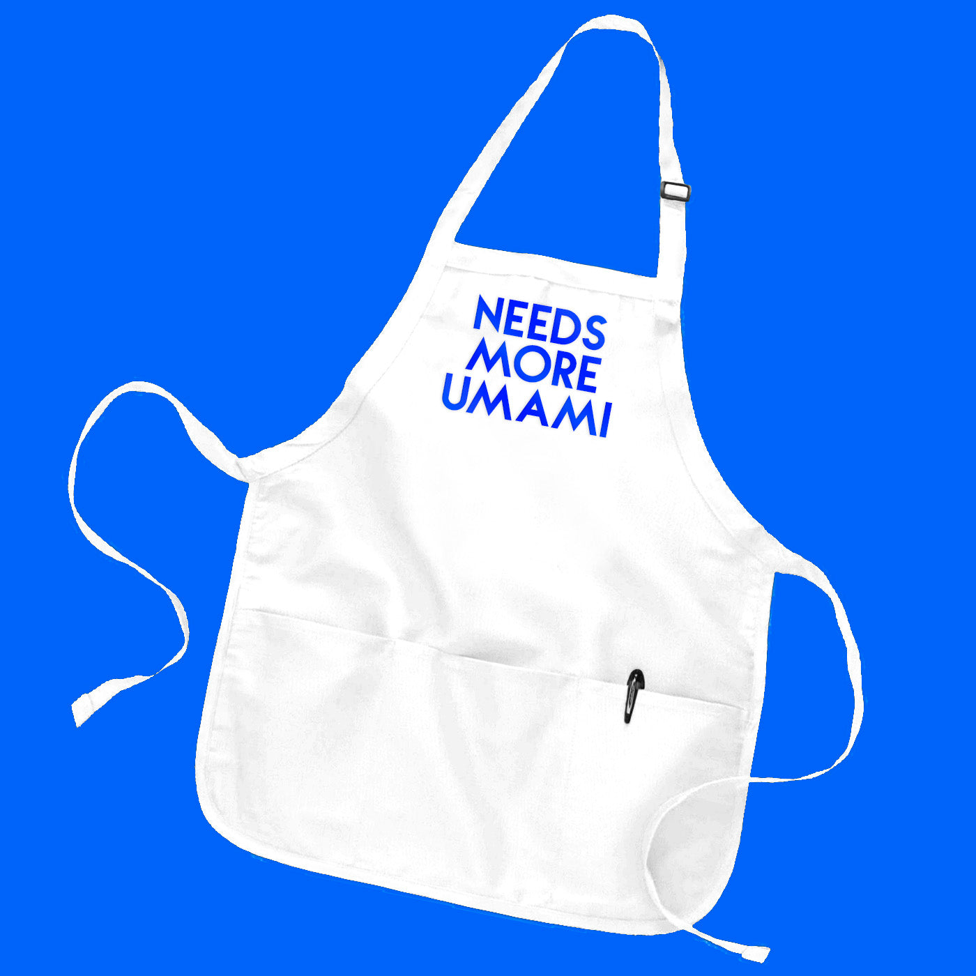 White baker-style apron with custom text "Needs More Umami" in blue metallic geometric text